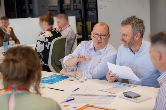 Two facilitators seated at a table in conversation with participants